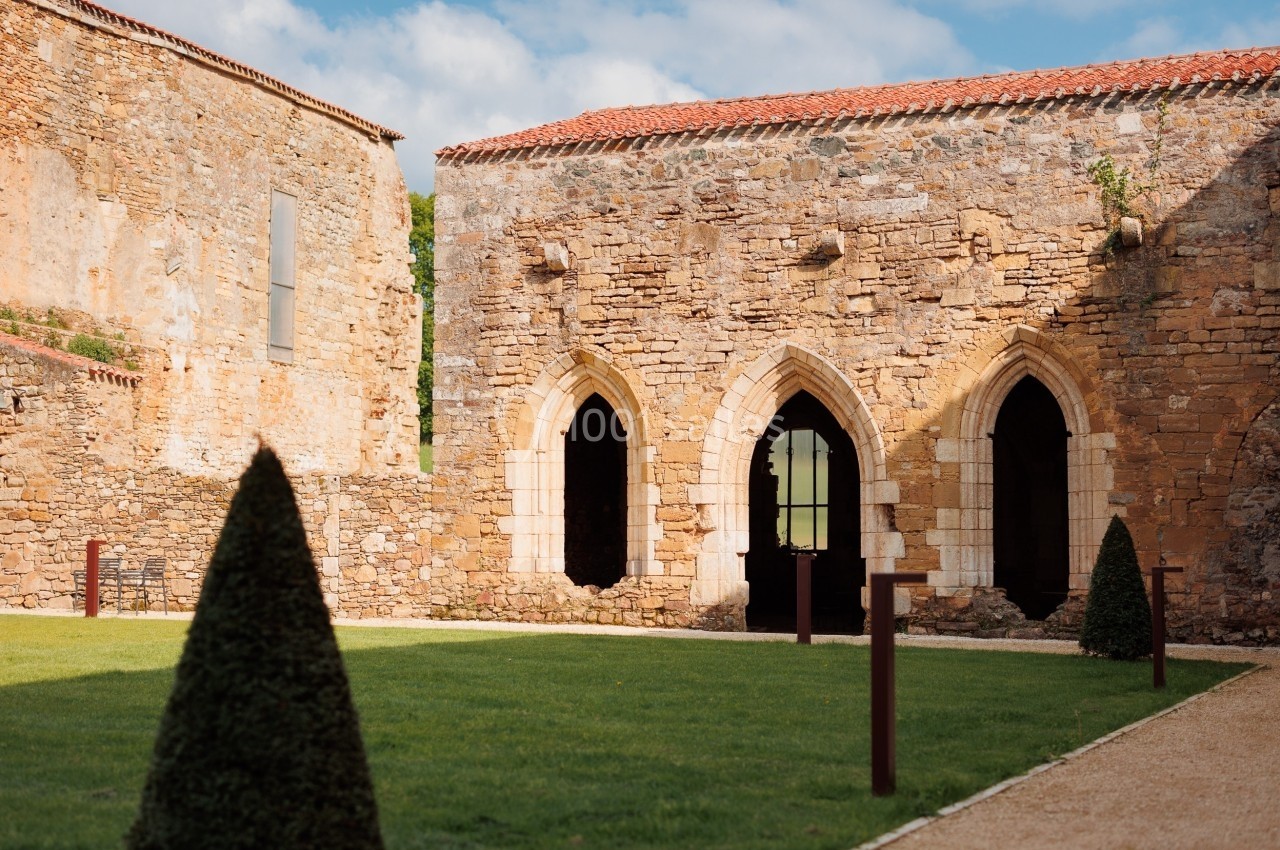 Vestiges d'un bâtiment en pierre avec arches gothiques, entouré d'une pelouse et de buissons taillés.
