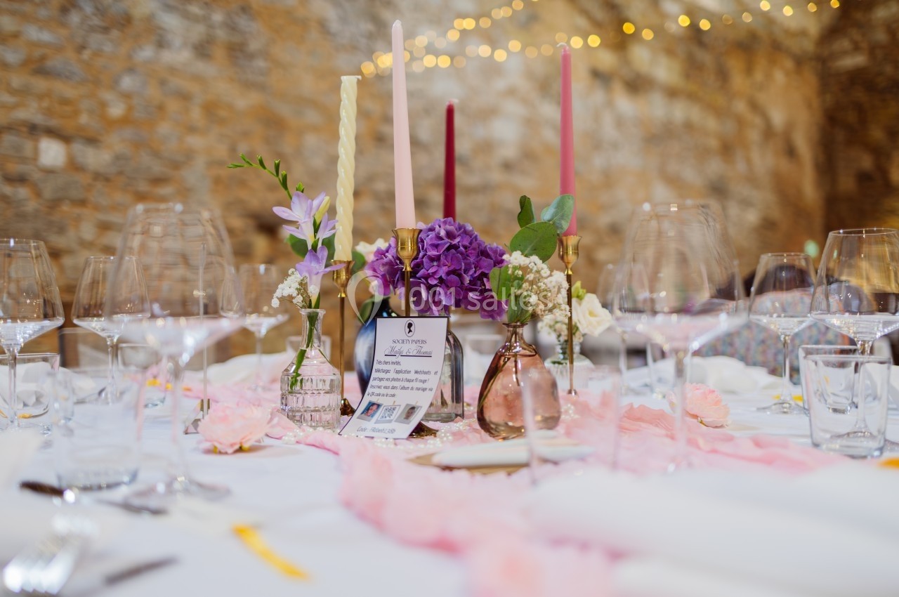 Table décorée pour un événement, ornée de fleurs, bougies colorées et vaisselle élégante dans un cadre en pierre.