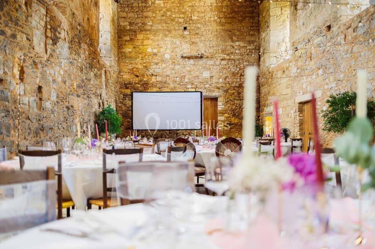 Salle en pierre aménagée pour un événement, avec tables décorées et un écran blanc en fond.
