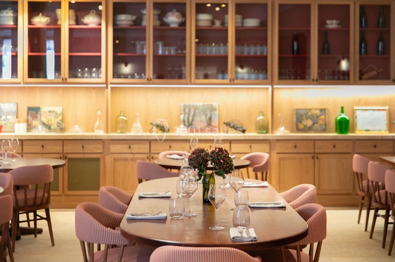 Salle de restaurant lumineuse avec tables en bois, chaises rembourrées roses et étagères garnies d'objets décoratifs.