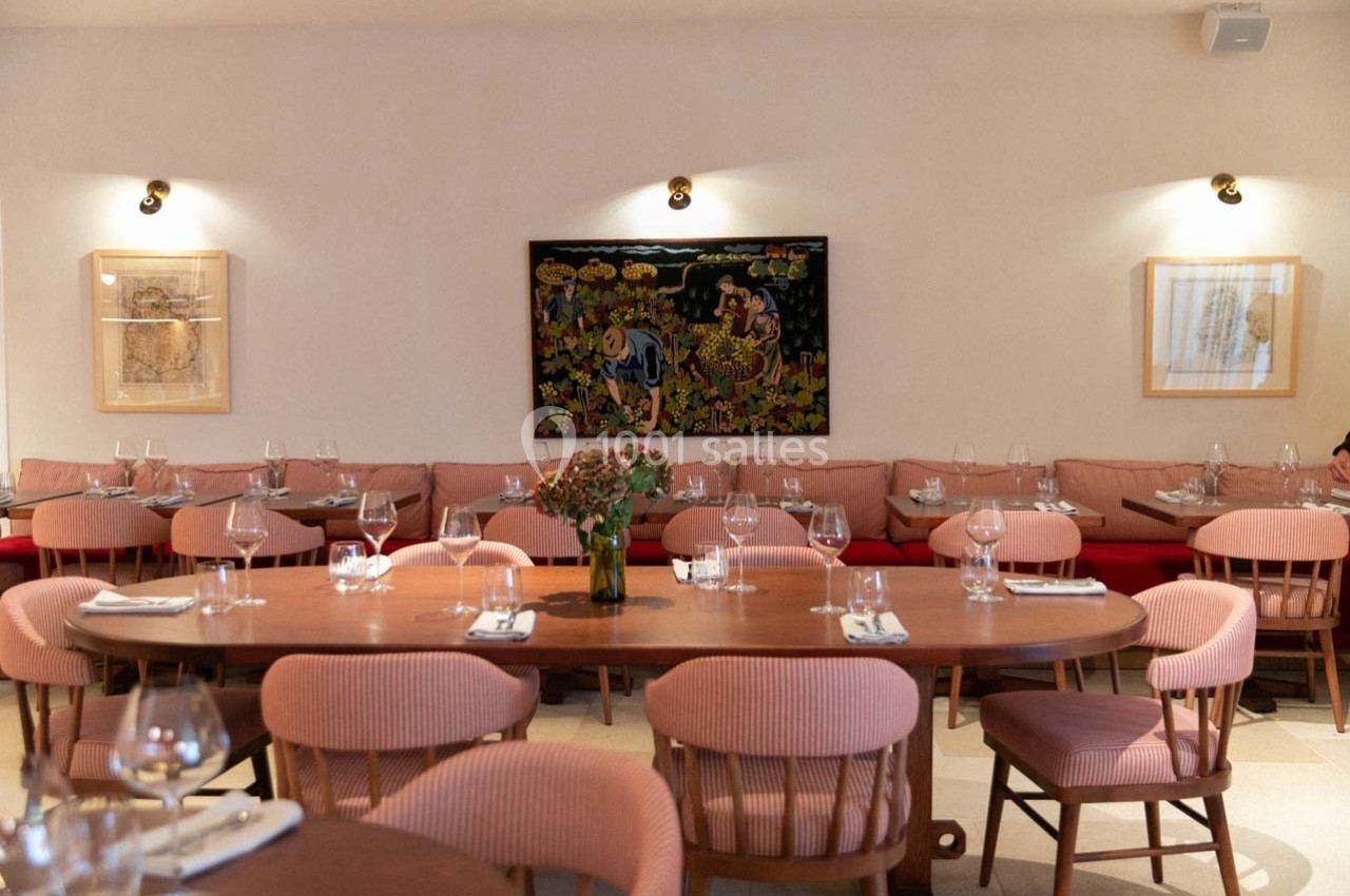 Salle de restaurant lumineuse avec tables en bois, chaises roses, banquettes rouges et tableaux accrochés aux murs.