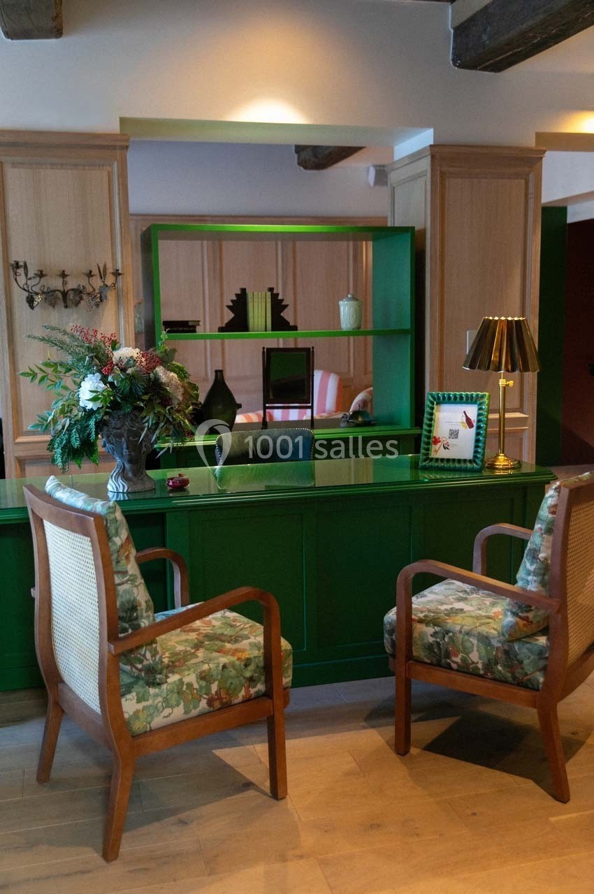 Bureau avec comptoir vert, deux fauteuils à motifs, étagères décorées et bouquet de fleurs dans un intérieur chaleureux.