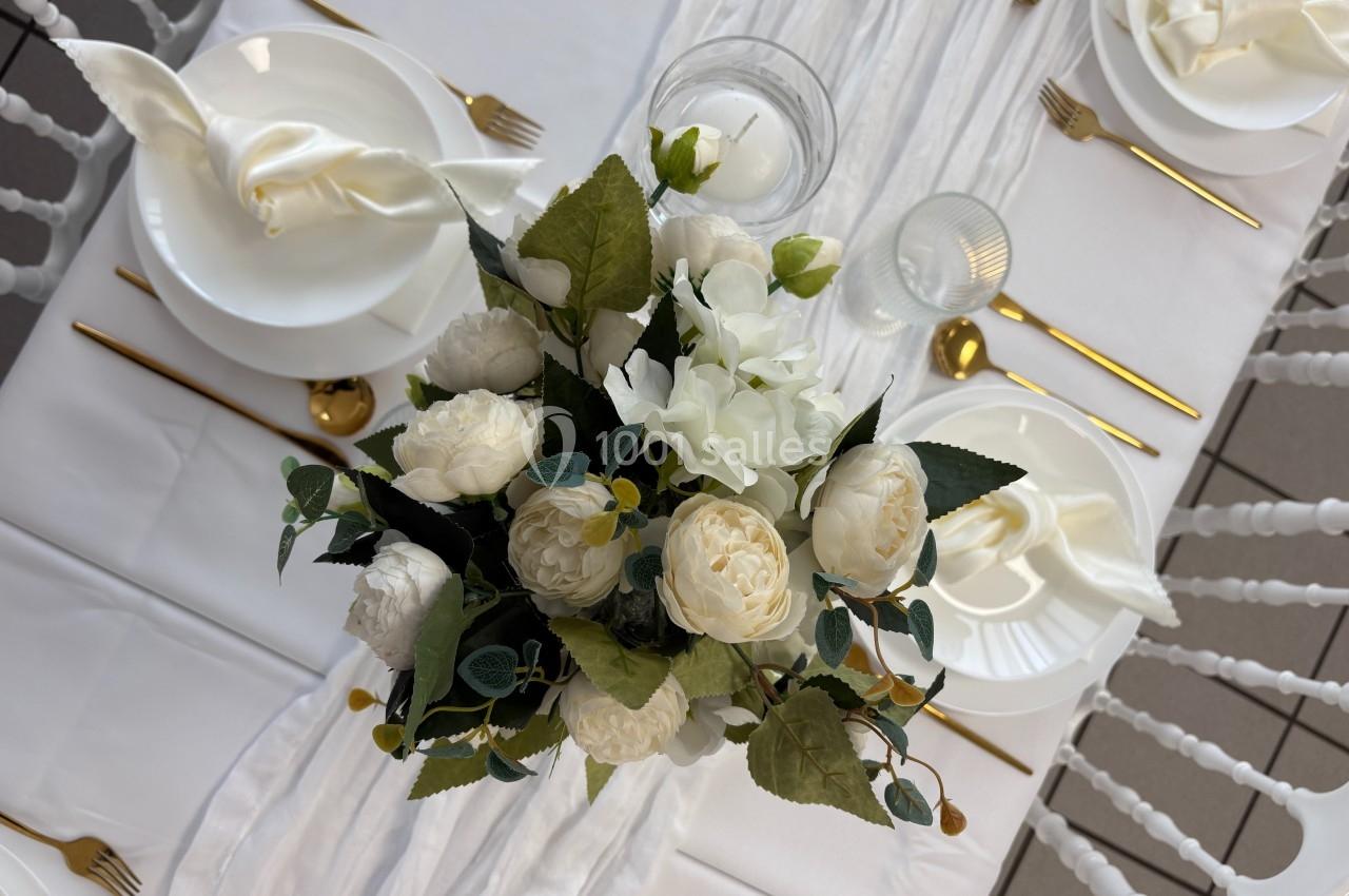 Vue d'une table élégamment dressée avec des couverts dorés, des assiettes blanches et un bouquet de fleurs blanches au…
