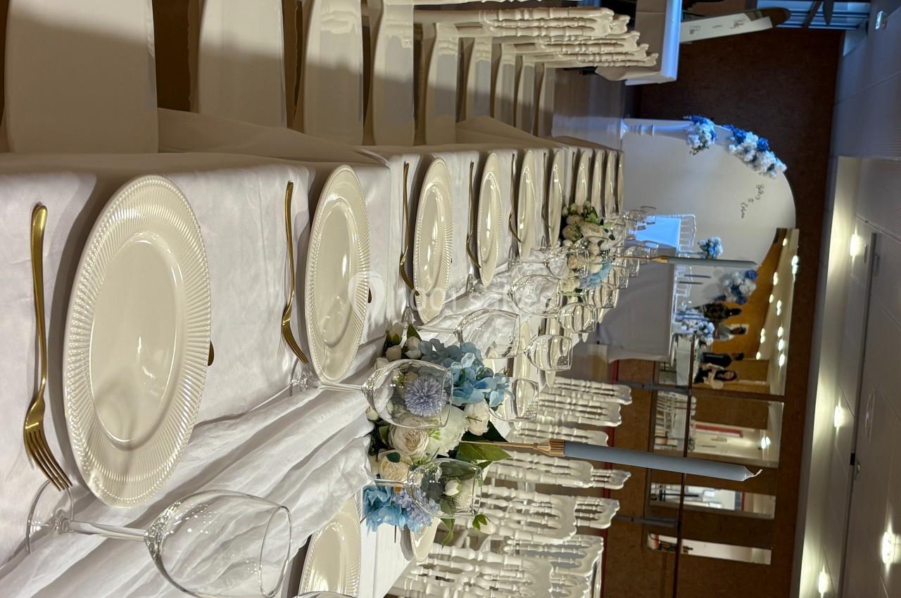 Table de réception élégamment dressée avec vaisselle blanche, couverts dorés et décorations florales bleues et blanches.