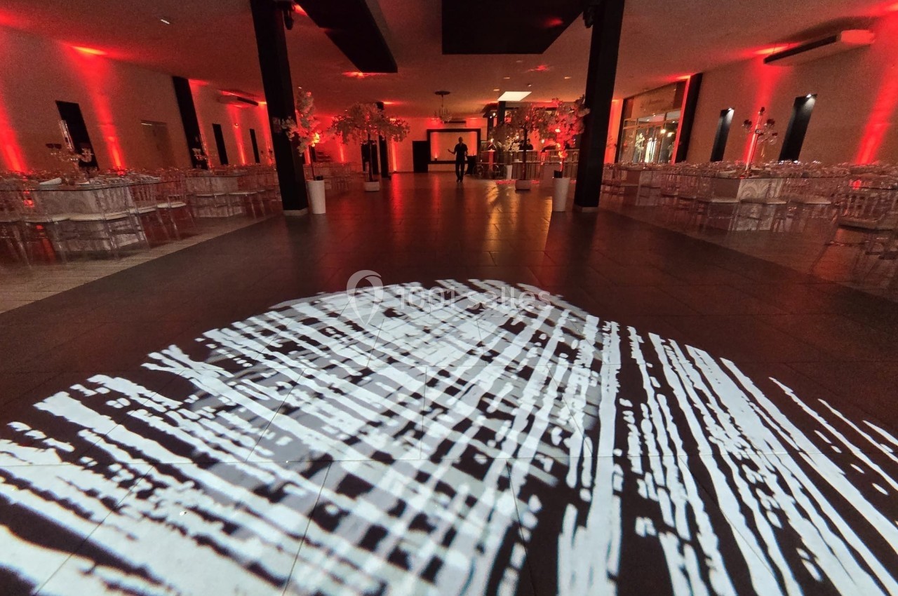 Salle de réception décorée avec des lumières rouges, tables dressées et projection lumineuse au sol.