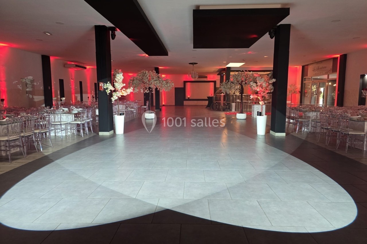 Salle de réception décorée avec des tables dressées, des chaises transparentes et des éclairages rouges.
