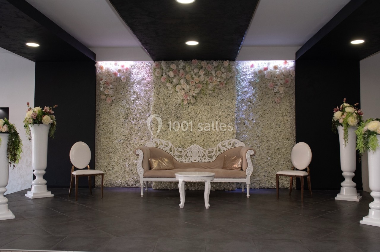 Salon décoré avec un canapé blanc orné, des chaises assorties et un mur floral en arrière-plan.