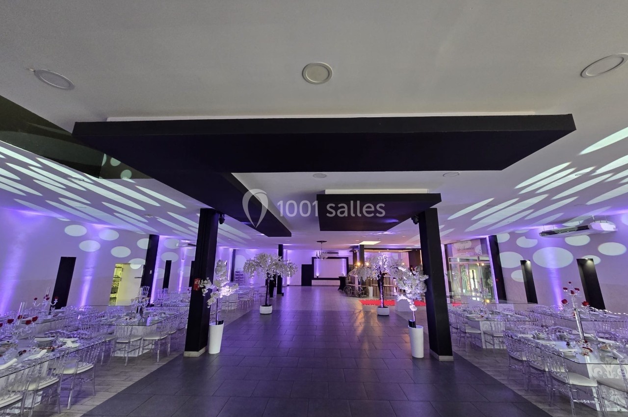 Salle de réception moderne avec tables décorées, chaises transparentes et éclairage violet diffus.