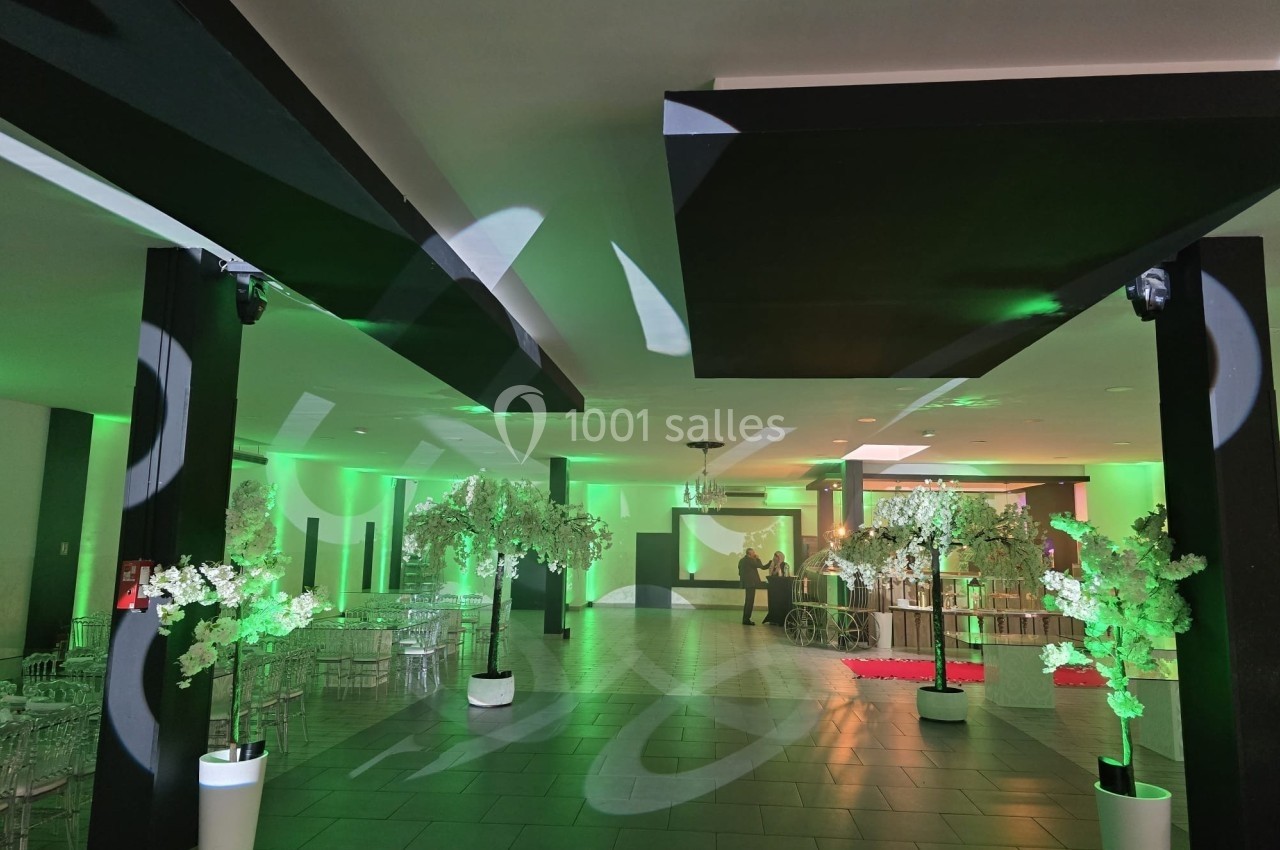 Salle de réception décorée avec des arbres artificiels illuminés de vert et des jeux de lumière sur le plafond.