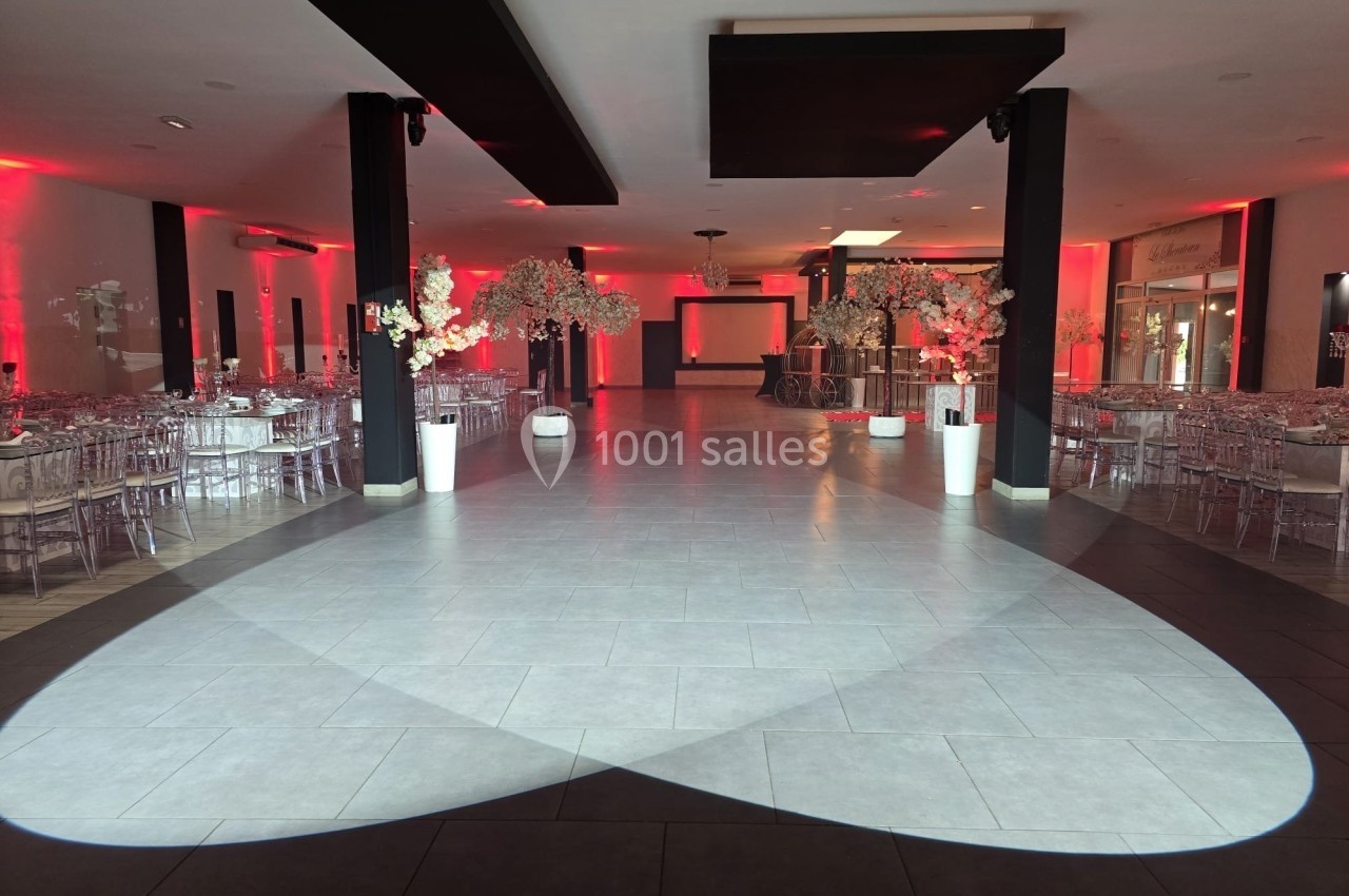Salle de réception décorée avec des tables dressées, des chaises transparentes et des éclairages rouges.