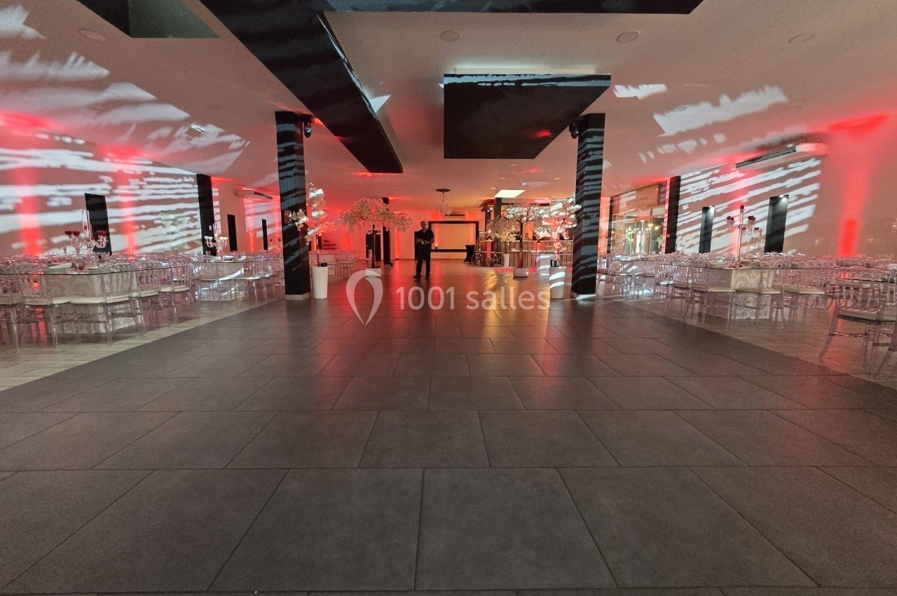 Salle de réception spacieuse avec éclairage rouge et blanc, tables décorées et chaises transparentes.