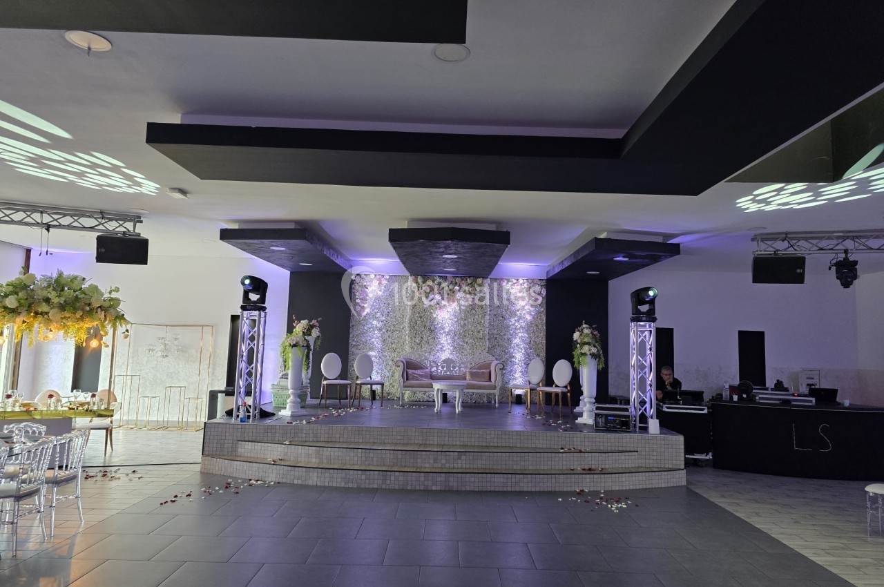 Salle de réception décorée avec une scène centrale, éclairage tamisé et arrangements floraux élégants.