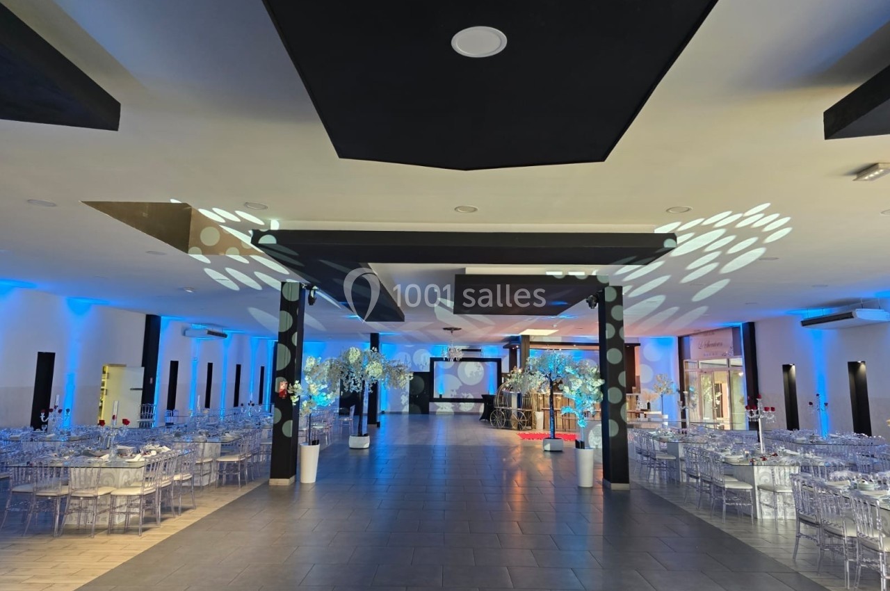 Salle de réception spacieuse avec tables dressées, éclairage bleu et décorations lumineuses modernes.