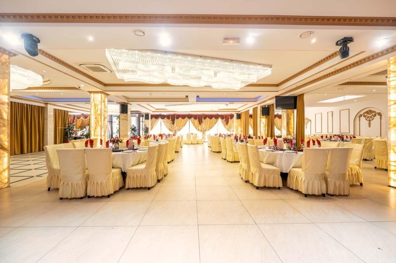 Salle de réception élégante avec tables dressées, chaises couvertes et lustres suspendus, prête pour un événement.