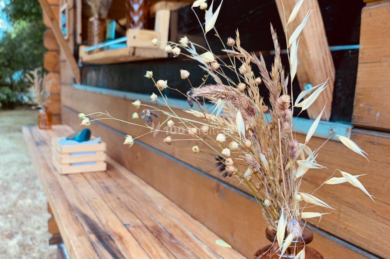 Bouquet de fleurs séchées posé sur une table en bois devant une cabane en bois avec des étagères décoratives.