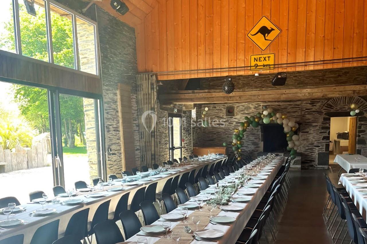Grande salle de réception avec longues tables dressées, décorée de ballons et d'un panneau mural avec un kangourou.