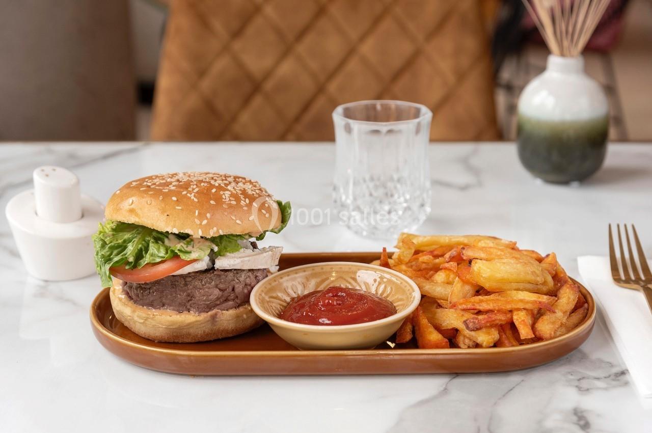 Assiette contenant un burger garni, des frites et une coupelle de ketchup, posée sur une table en marbre.