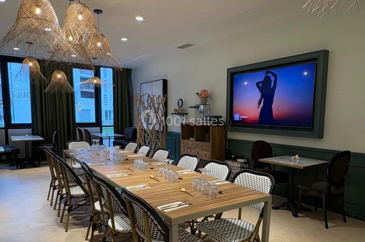 Salle de restaurant élégante avec une grande table dressée, des chaises en osier et un écran affichant une silhouette au…