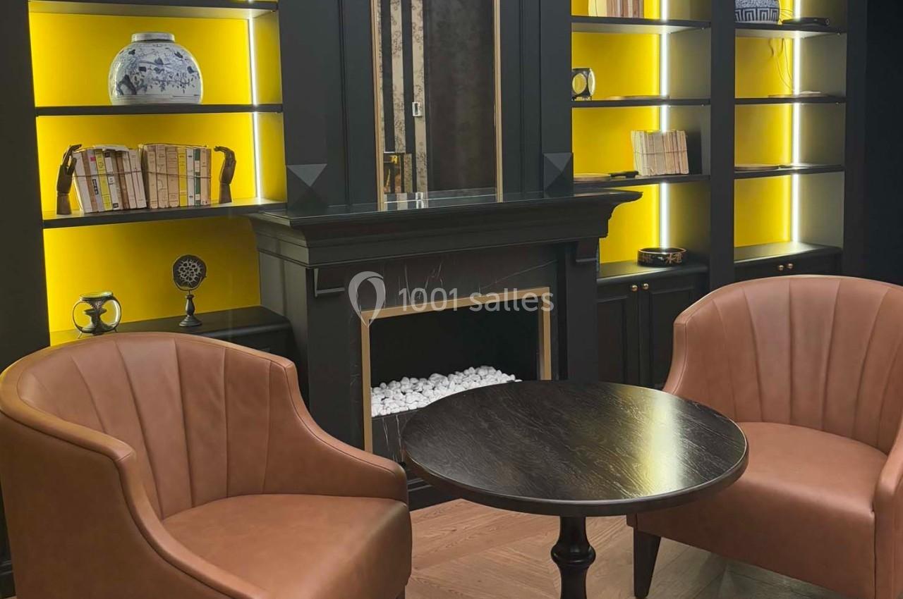 Deux fauteuils en cuir marron entourent une table ronde devant une cheminée encadrée d'étagères éclairées.