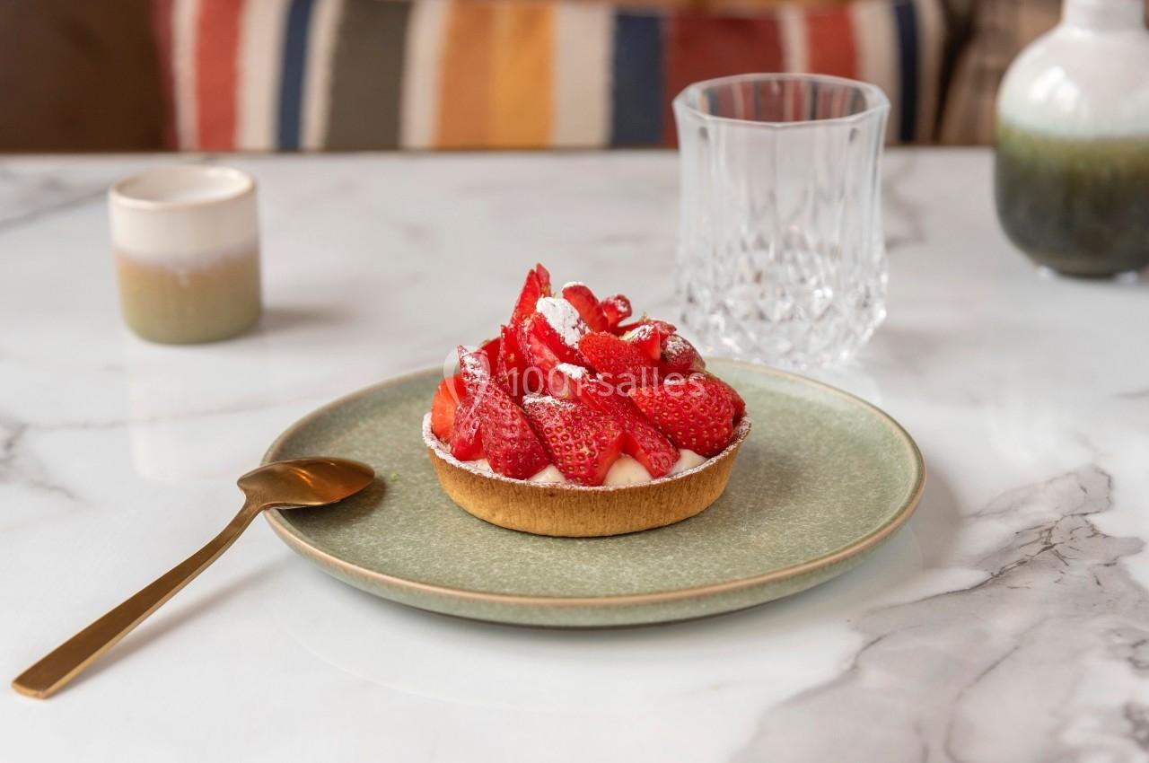 Tartelette aux fraises garnie de fruits frais et saupoudrée de sucre glace, servie sur une assiette verte.
