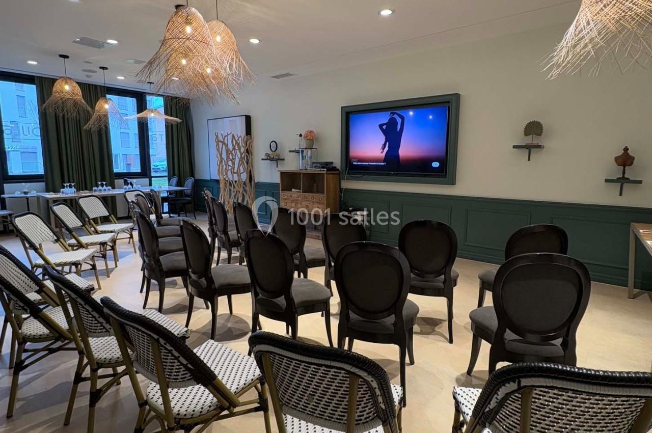 Salle de réunion équipée de chaises alignées, d'un écran affichant une silhouette et de luminaires suspendus.