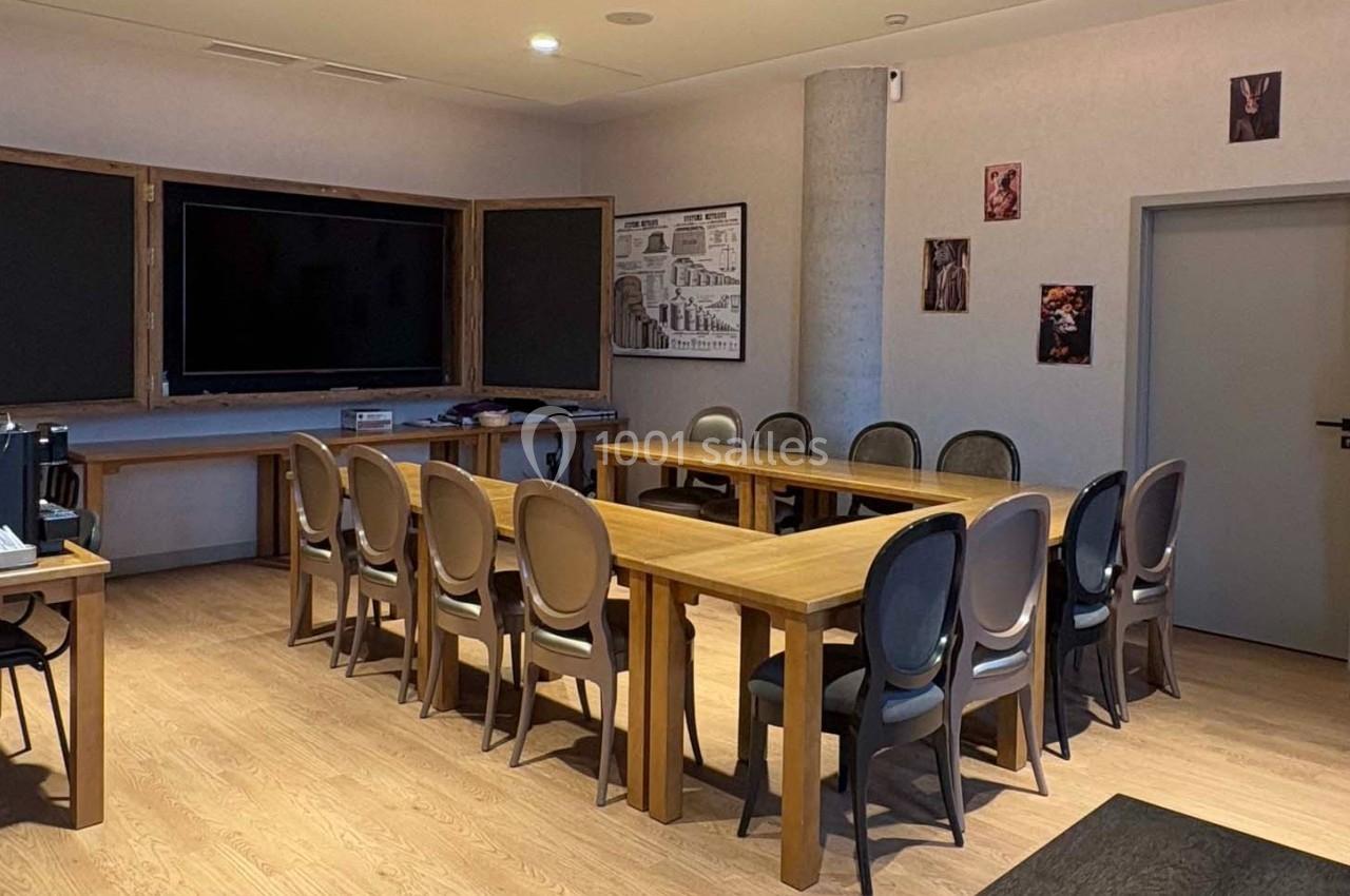 Salle de réunion avec tables en bois disposées en U, chaises grises, écran mural et décorations sur les murs.
