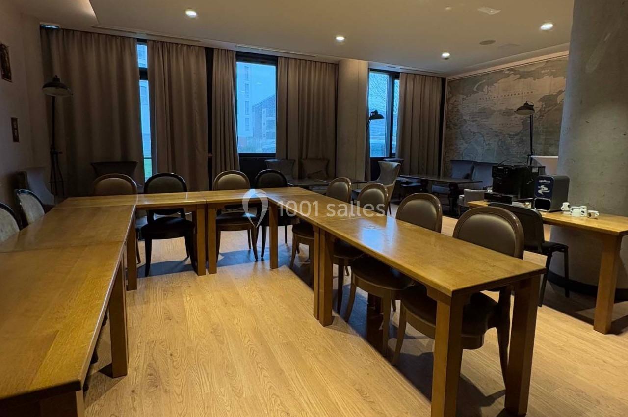 Salle de réunion avec tables en bois disposées en U, chaises assorties et grandes fenêtres avec rideaux.