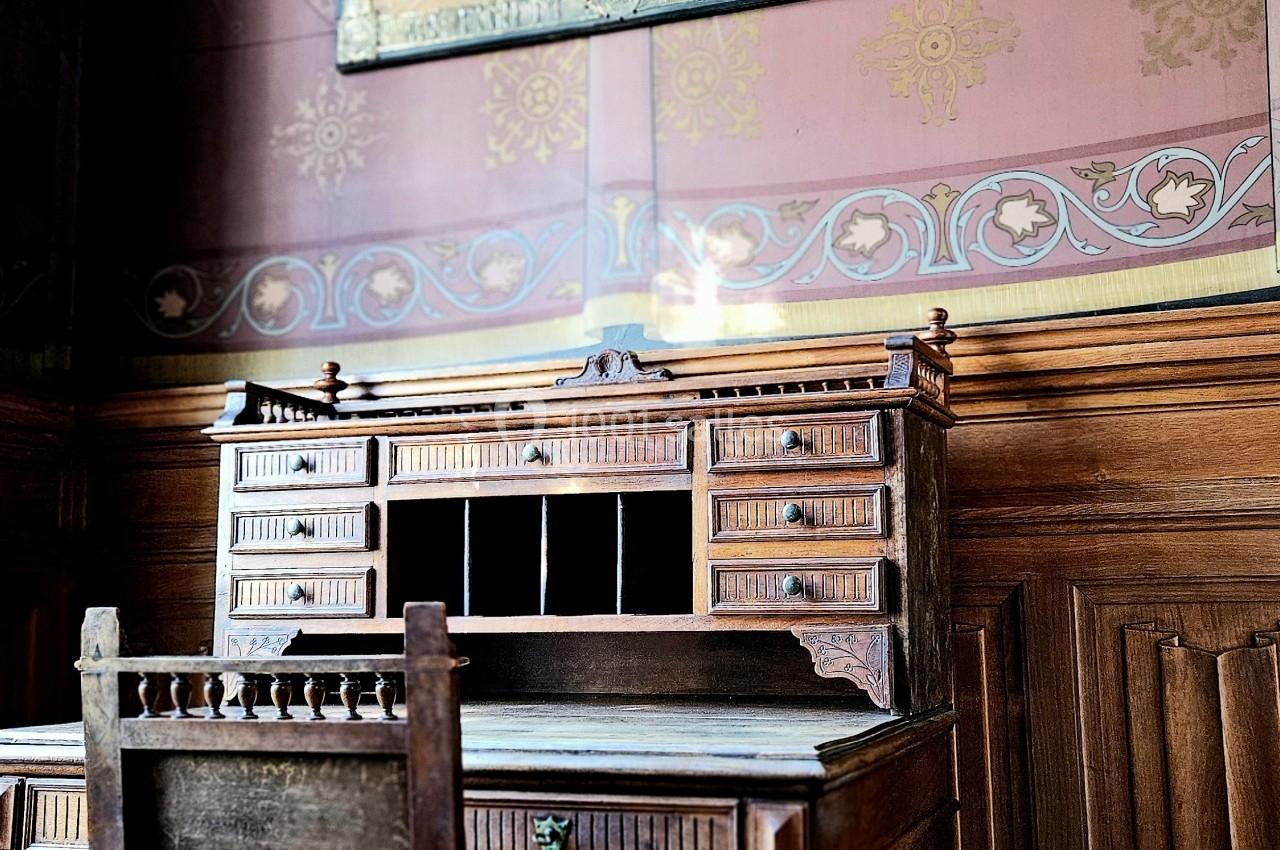 Bureau en bois ancien avec une chaise assortie, devant un mur décoré et un tableau encadré suspendu.