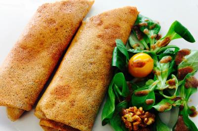 Un food truck servant des crêpes dans un parc avec des tables et des clients assis ou en file d'attente.