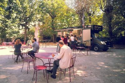 Un food truck servant des crêpes dans un parc avec des tables et des clients assis ou en file d'attente.