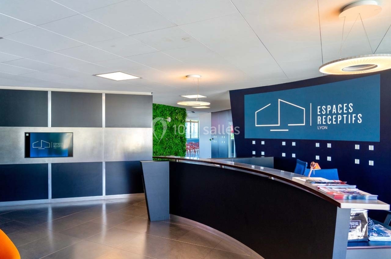 Location salle Caluire-et-Cuire (Rhône) - Le Belvédère #6 Accueil moderne avec comptoir noir, mur végétal, écran mural et logo ’Espaces Réceptifs Lyon’ en arrière-plan.