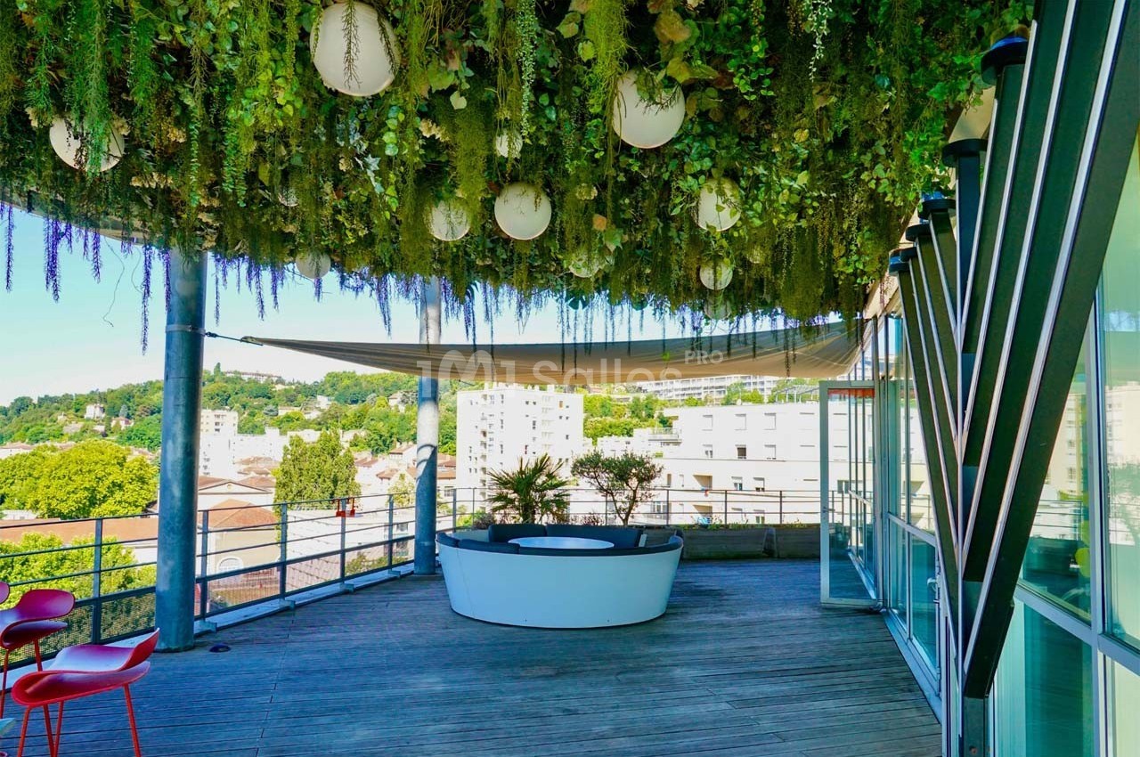 Terrasse avec plafond végétalisé, luminaires suspendus, mobilier moderne et vue sur des bâtiments urbains.