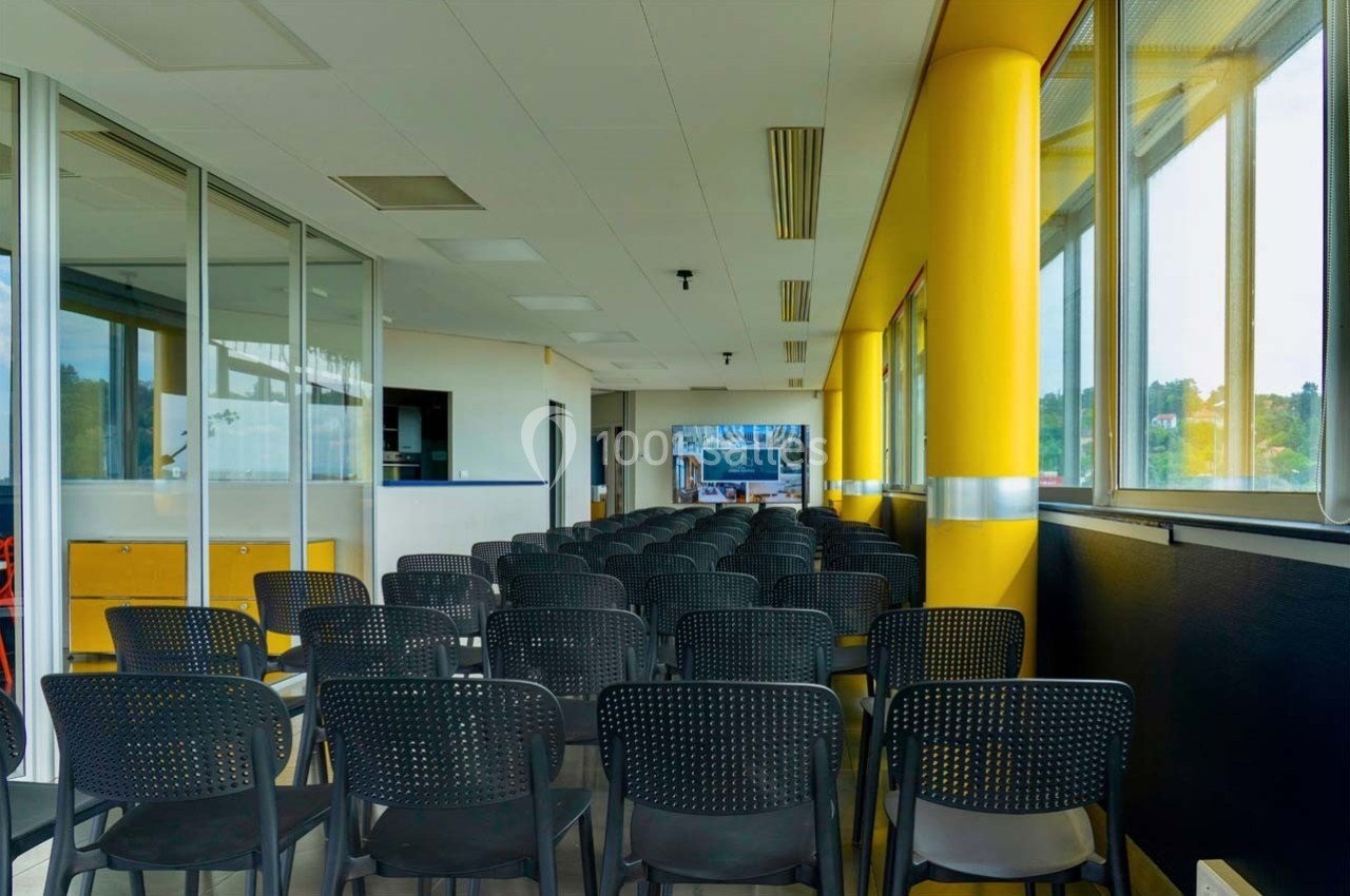 Location salle Caluire-et-Cuire (Rhône) - Le Belvédère #16 Salle de conférence lumineuse avec rangées de chaises noires alignées face à un écran au fond de la pièce.