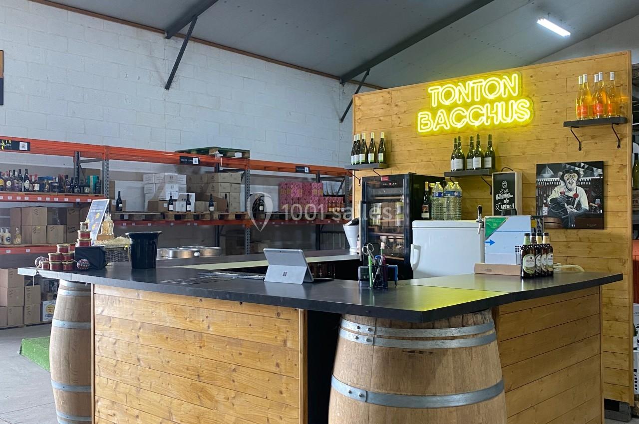 Comptoir en bois avec tonneaux, situé dans un espace de vente, éclairé par un néon ’Tonton Bacchus’.
