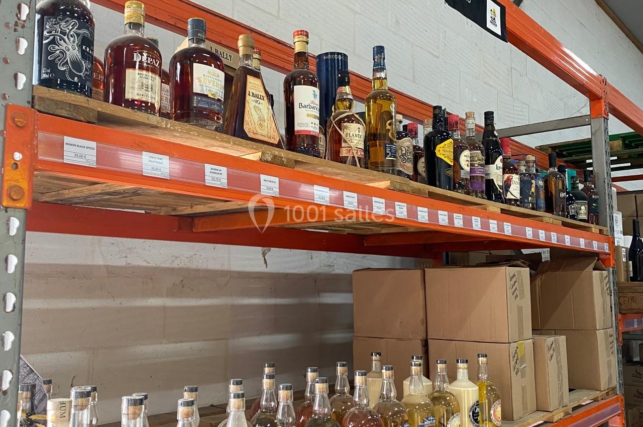 Étagères métalliques contenant diverses bouteilles d'alcool, alignées dans un entrepôt avec des cartons en dessous.