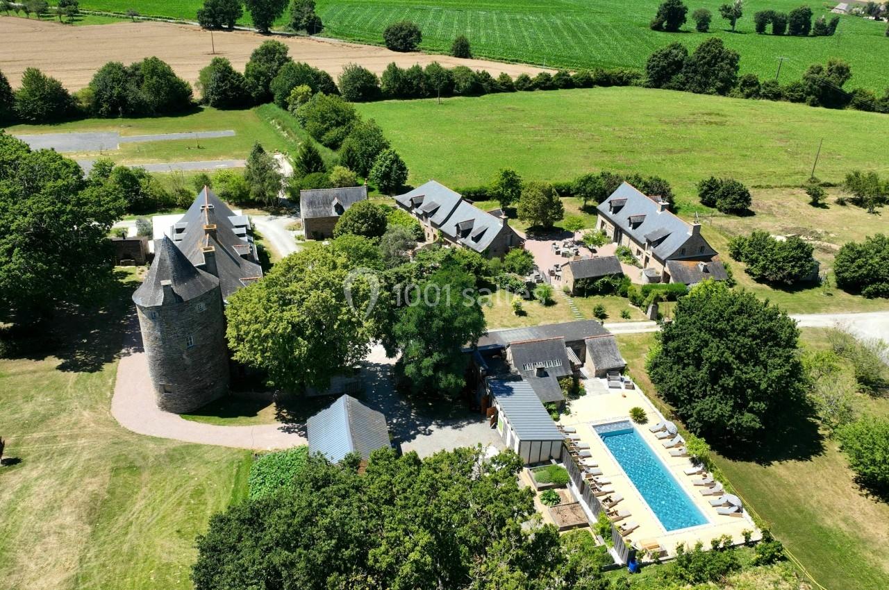 Vue aérienne d'un domaine rural avec piscine, bâtiments en pierre, tour ancienne et espaces verts environnants.