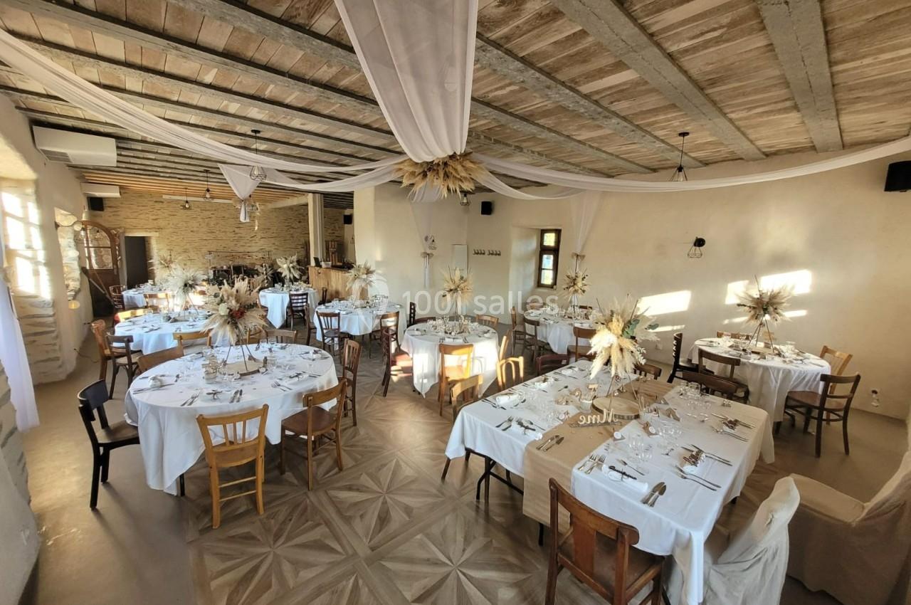 Salle de réception décorée avec des tables dressées, des chaises variées et des ornements floraux sous un plafond en bois.