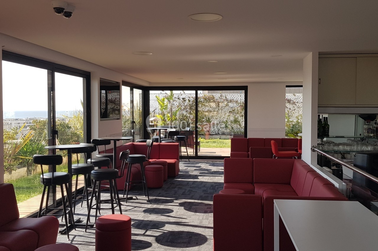 Salle lumineuse avec mobilier rouge et noir, grandes baies vitrées donnant sur un espace extérieur verdoyant.