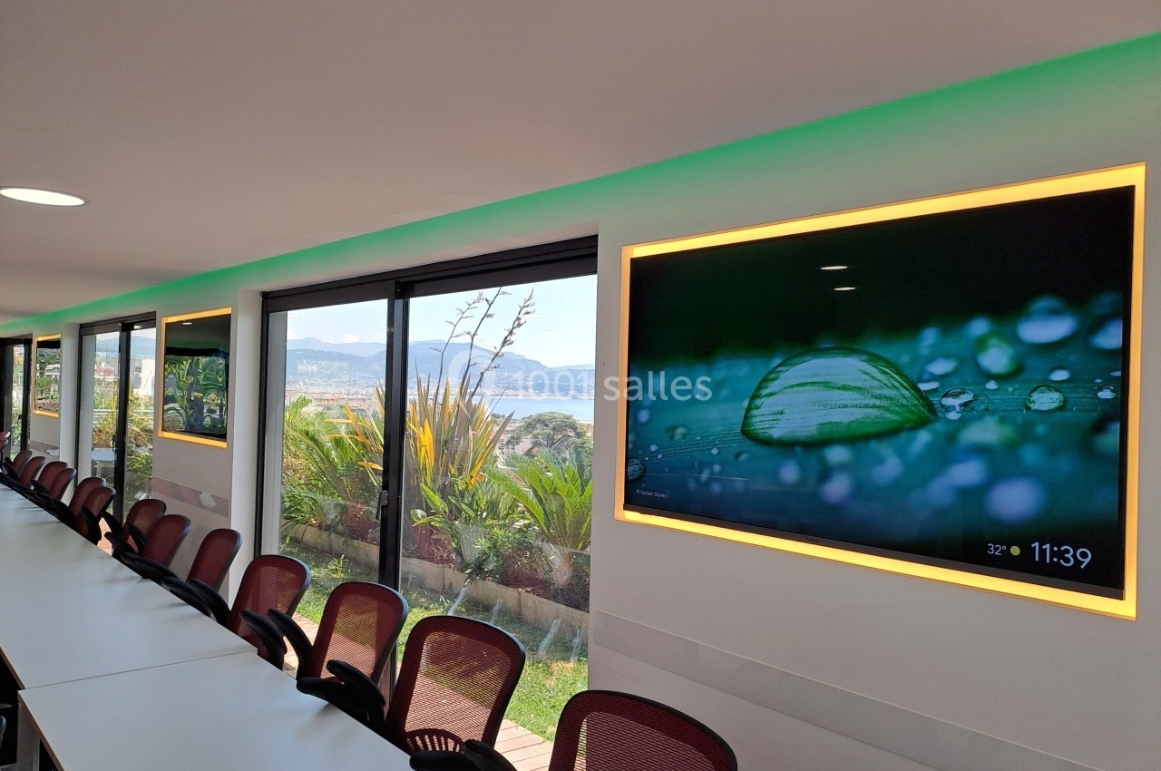 Salle de réunion lumineuse avec une grande table, des chaises et des écrans affichant des images de nature.