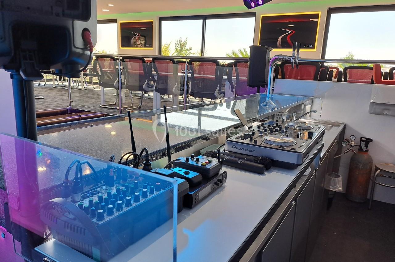 Poste de DJ avec table de mixage, platines et équipements audio, installé dans un espace lumineux avec des sièges en arrière…