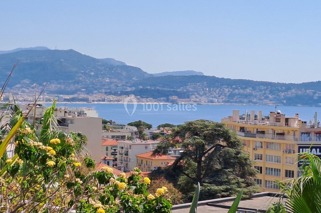 Vue sur des bâtiments, des arbres et la mer Méditerranée avec des collines en arrière-plan sous un ciel dégagé.
