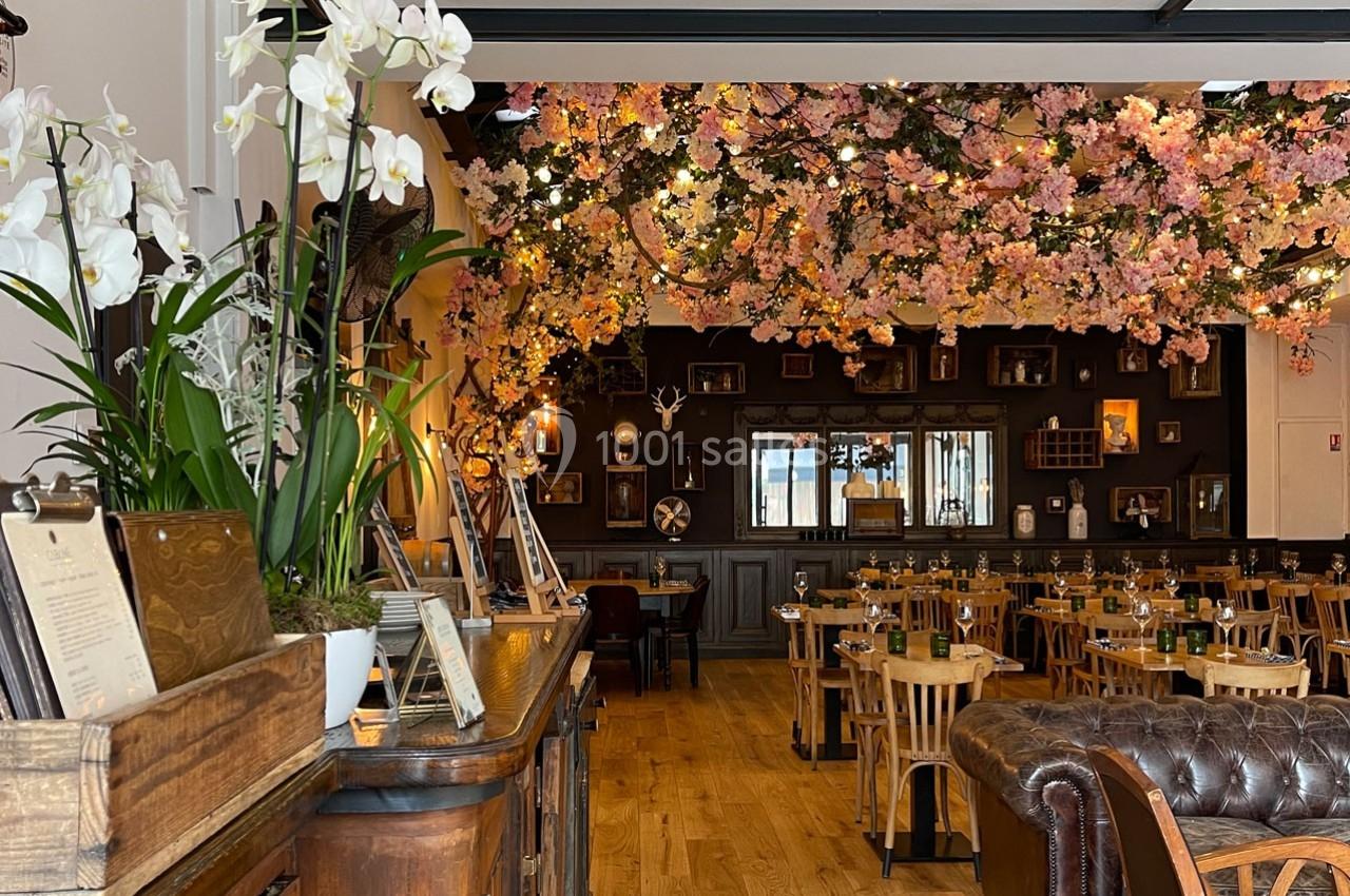 Salle de restaurant décorée avec des fleurs suspendues, des tables en bois et un comptoir avec des orchidées blanches.