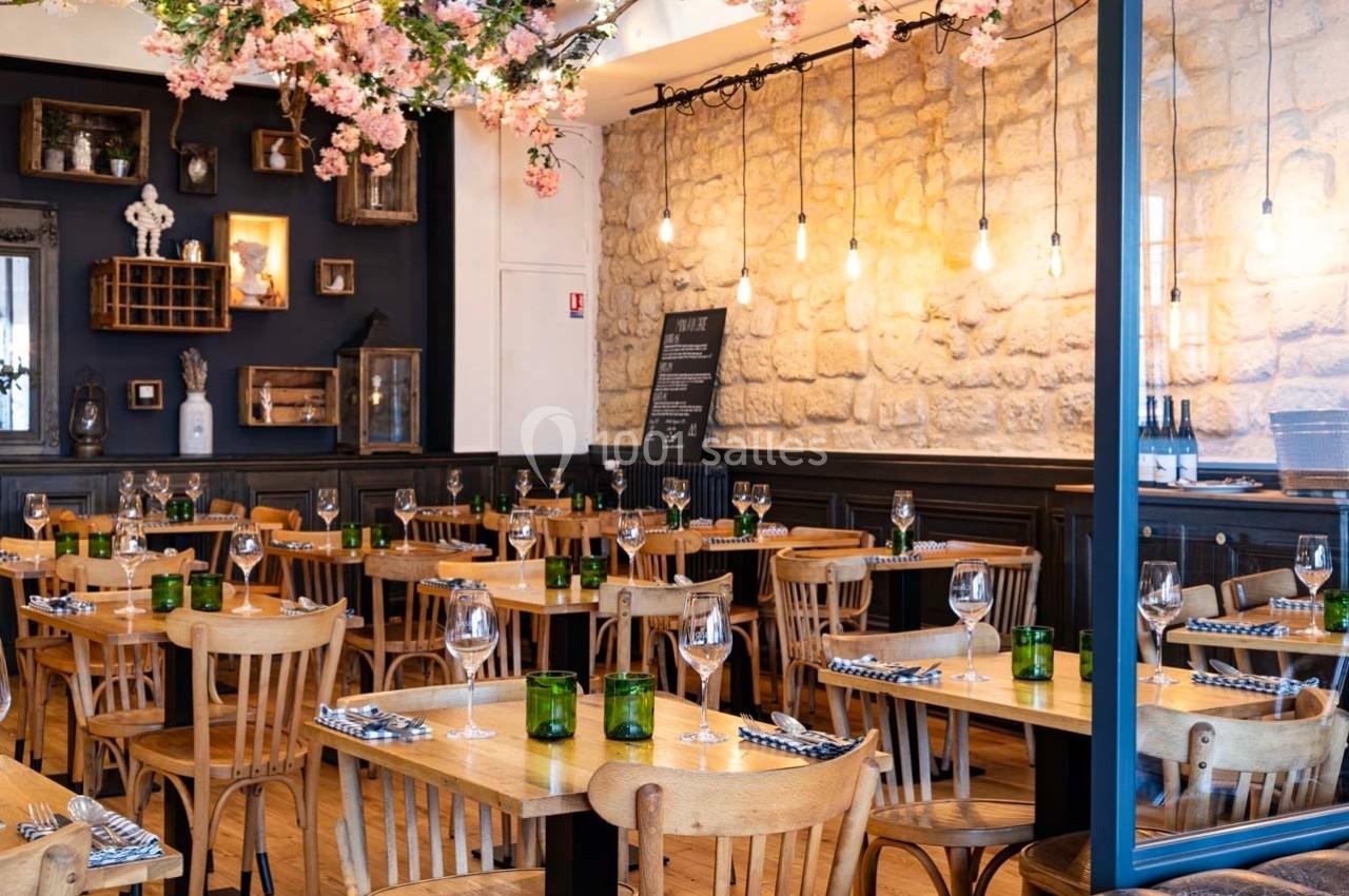 Salle de restaurant chaleureuse avec tables en bois, murs en pierre, décor floral et éclairage suspendu.