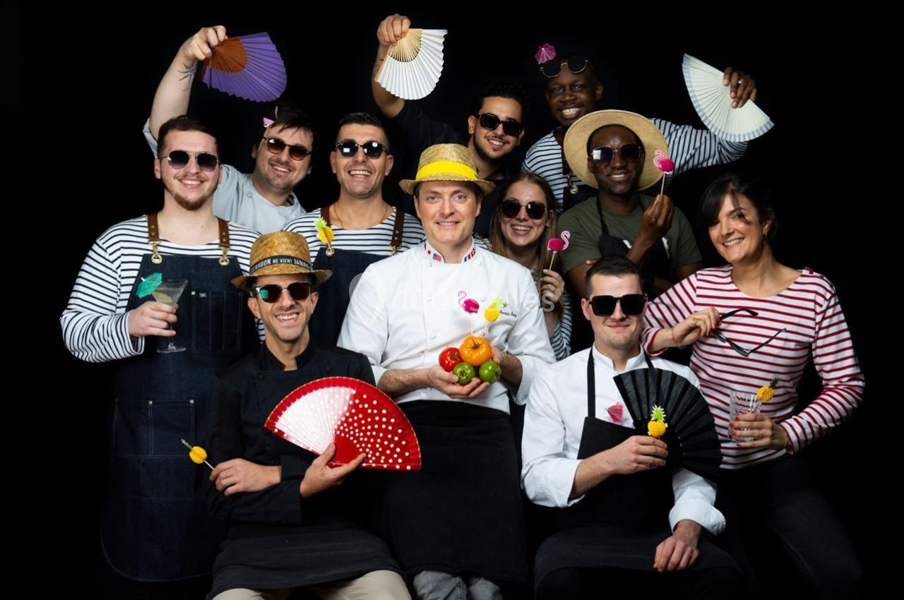 Un groupe de personnes souriantes en tenues variées posant avec des éventails, chapeaux et accessoires colorés.