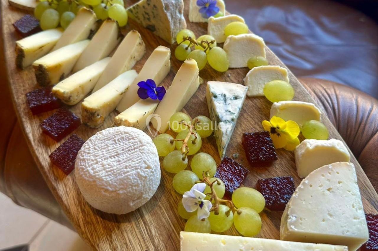 Plateau de fromages variés avec raisins, fleurs comestibles et morceaux de pâte de fruits sur une planche en bois.