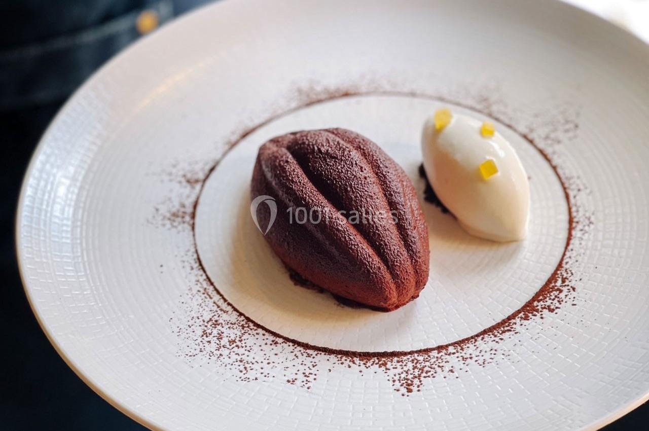 Dessert composé d'un entremets chocolaté en forme de fève de cacao, accompagné d'une quenelle de crème et zestes.