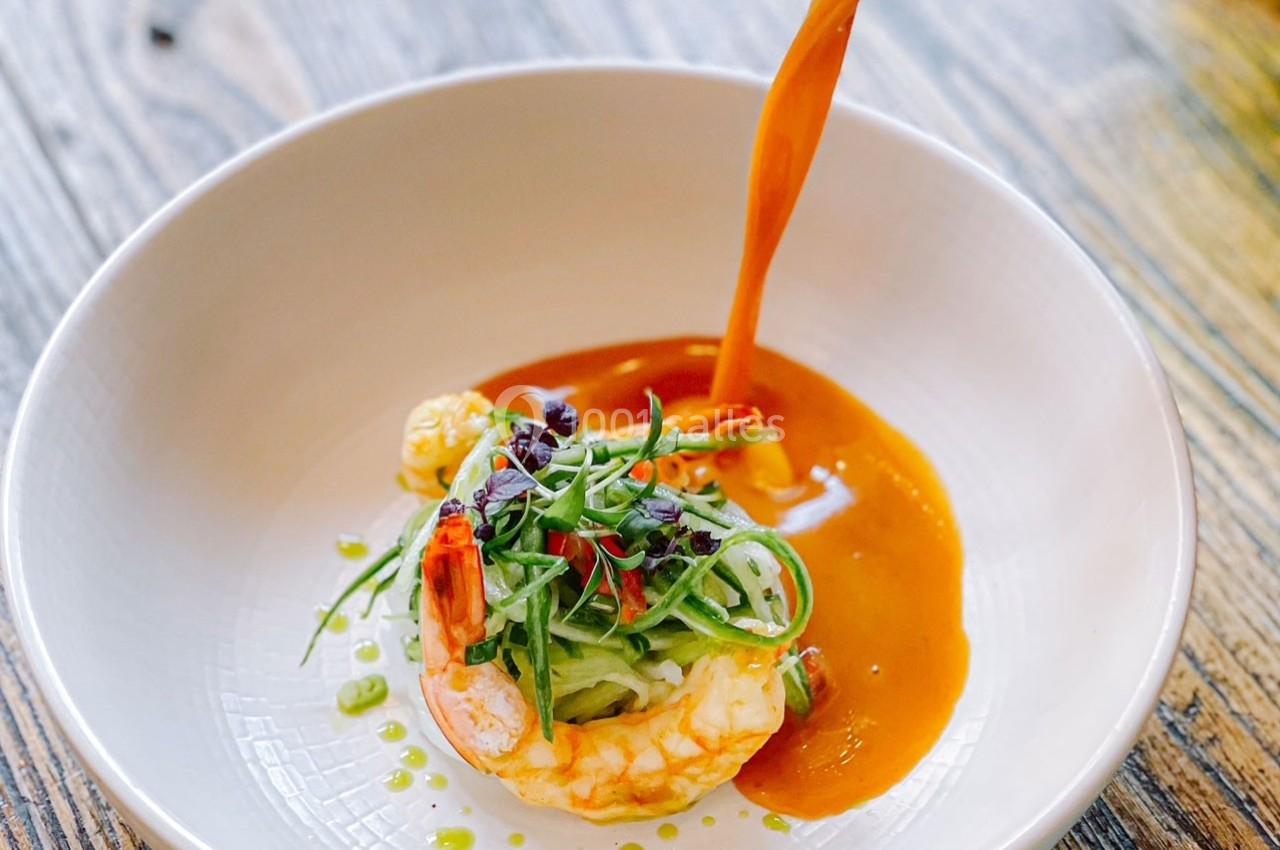 Crevette garnie de légumes verts et herbes fraîches, nappée de sauce orange dans une assiette blanche.