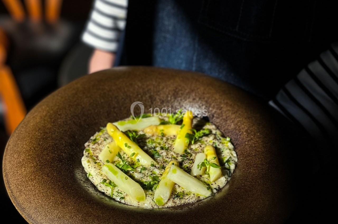 Assiette de purée garnie d'asperges blanches et jaunes, parsemée de fines herbes, présentée sur un fond sombre.