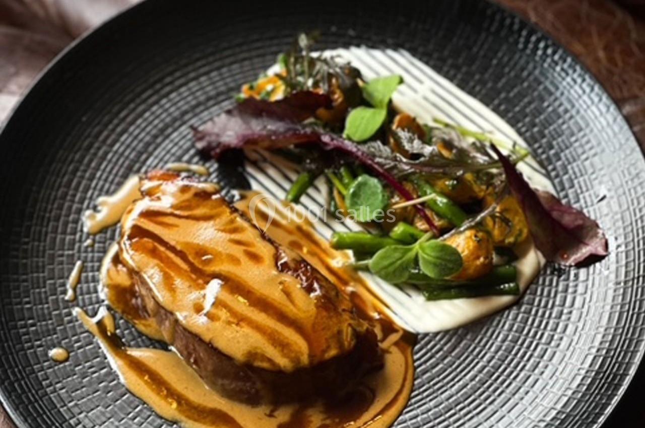 Assiette gastronomique avec viande nappée de sauce, accompagnée de légumes verts et purée dressée sur une assiette noire.