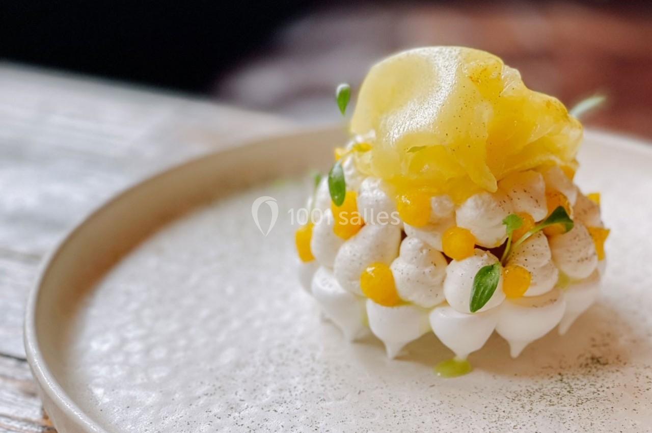 Dessert raffiné composé de meringue, crème et morceaux de fruits jaunes, présenté sur une assiette blanche.